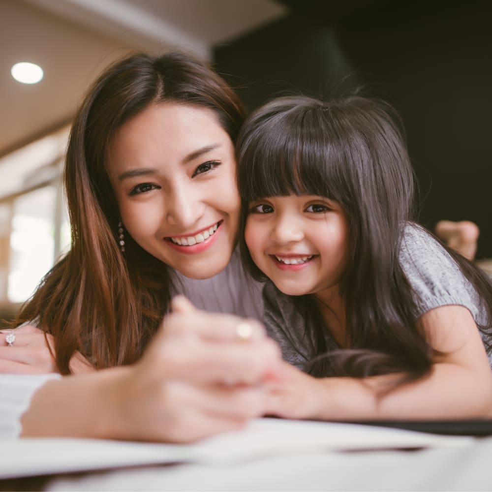 A woman and a young girl are hugging while laying on their stomachs.