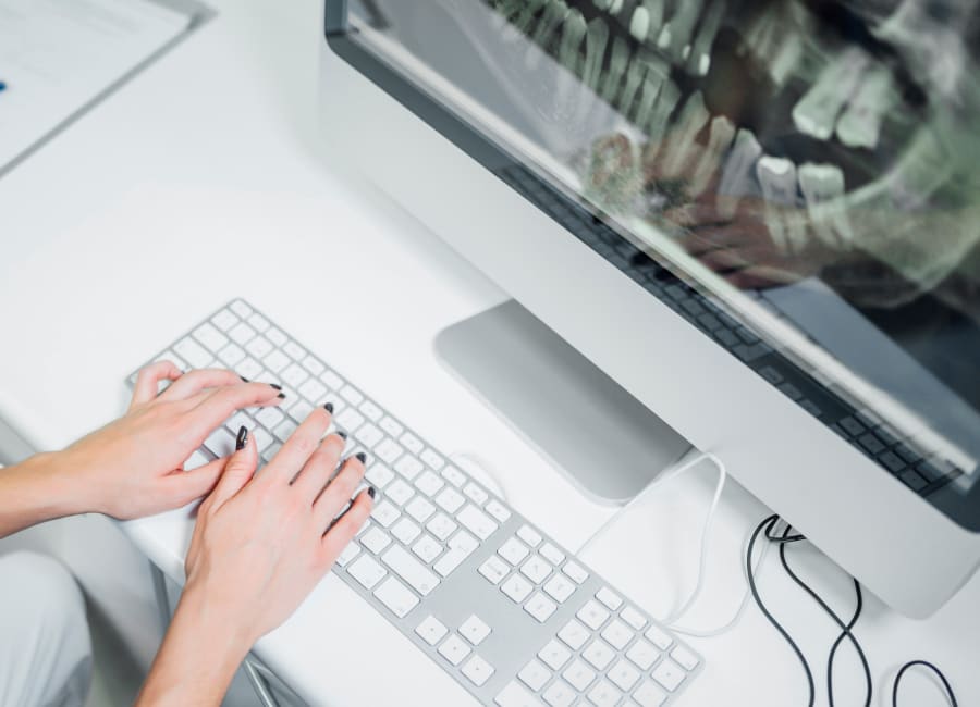 A computer monitor show a panoramic X-ray while a woman's hands rest on the keyboard.