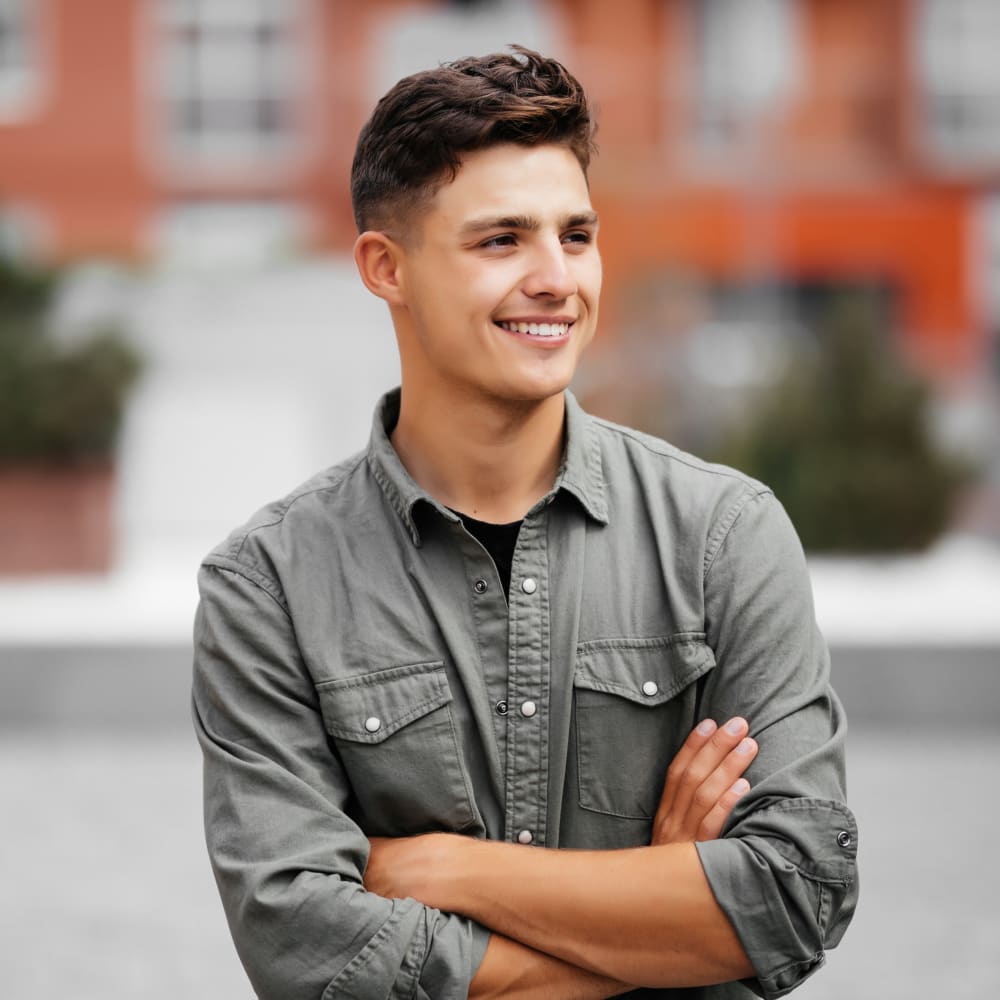 A teenage boy stands outside looking off to the side and smiling.