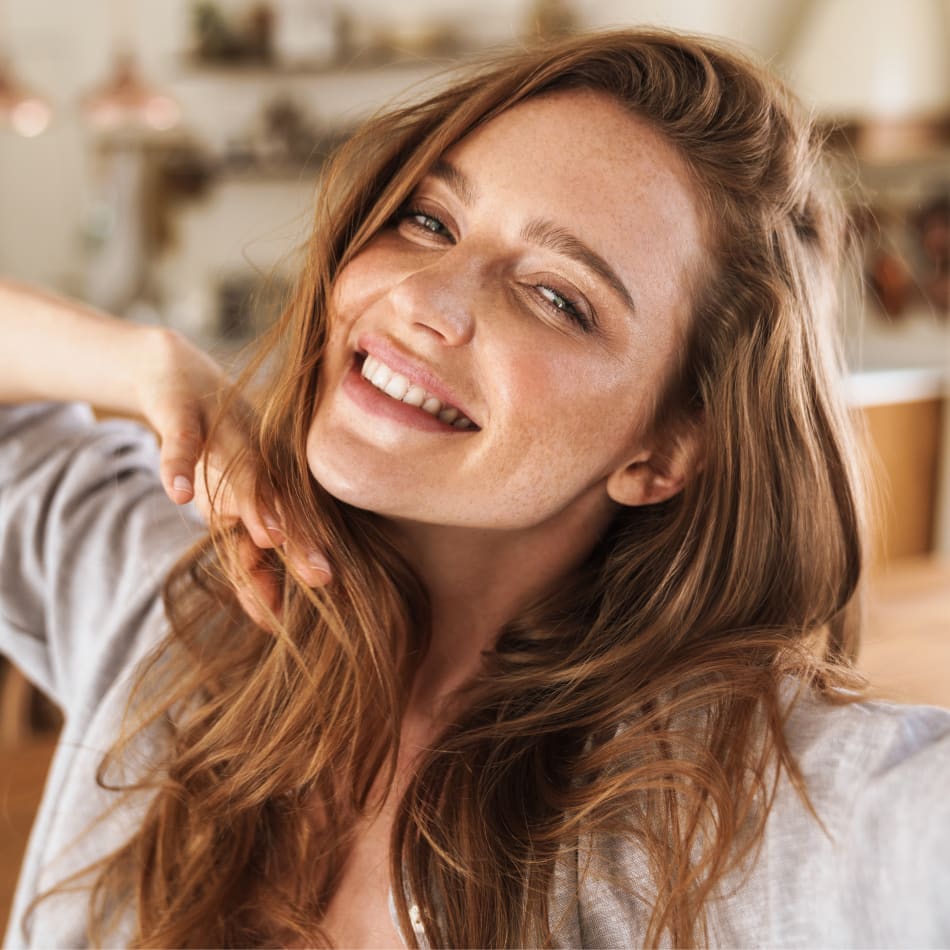 A teen girl stands smiling really wide while holding her hand under her chin.